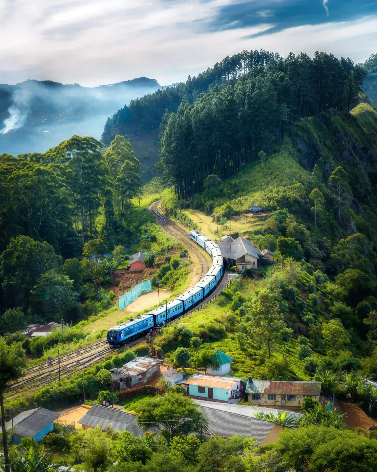 Blue hill country train curving through a village below forested ridges near Haputale, Sri Lanka