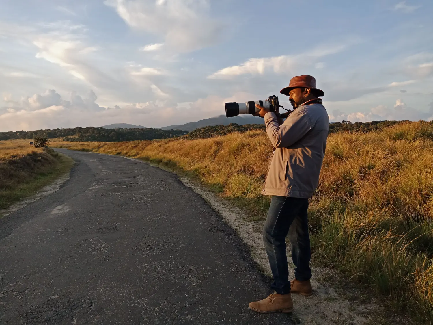 A photographer with a telephoto lens working beside the park road at Horton Plains in low golden light