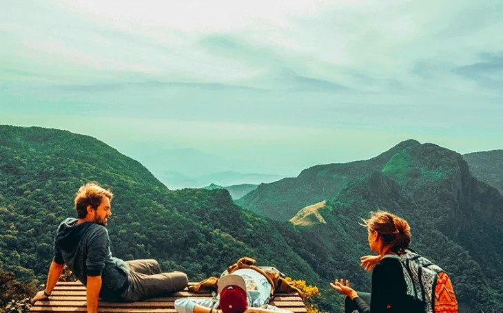 Hikers resting at the World's End viewpoint platform in Horton Plains, overlooking layered misty green ridges falling away toward the horizon